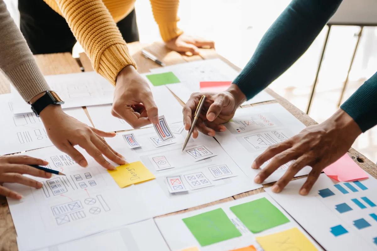 Hands arranging printed wireframes and coloured sticky notes on a table during a planning session